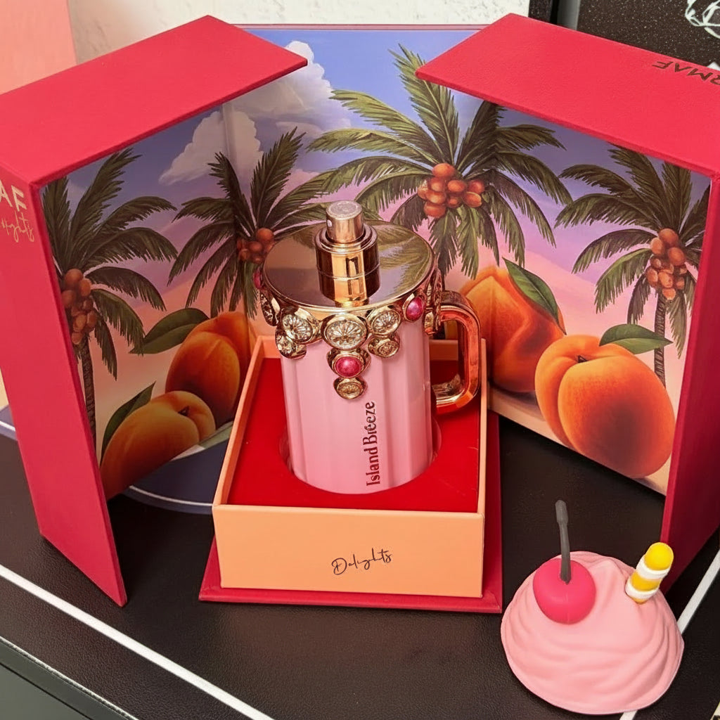 ARMAE Dolly perfume bottle displayed in its open red gift box, with a pink ceramic mug featuring a gold and rose-gold perfume atomizer on top. The box has illustrated beach scenery on the inside panels, and a small pink dessert-shaped accessory sits in front on a dark tabletop.