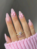 Hand with pink nail polish and rings, wearing a pink sweater.