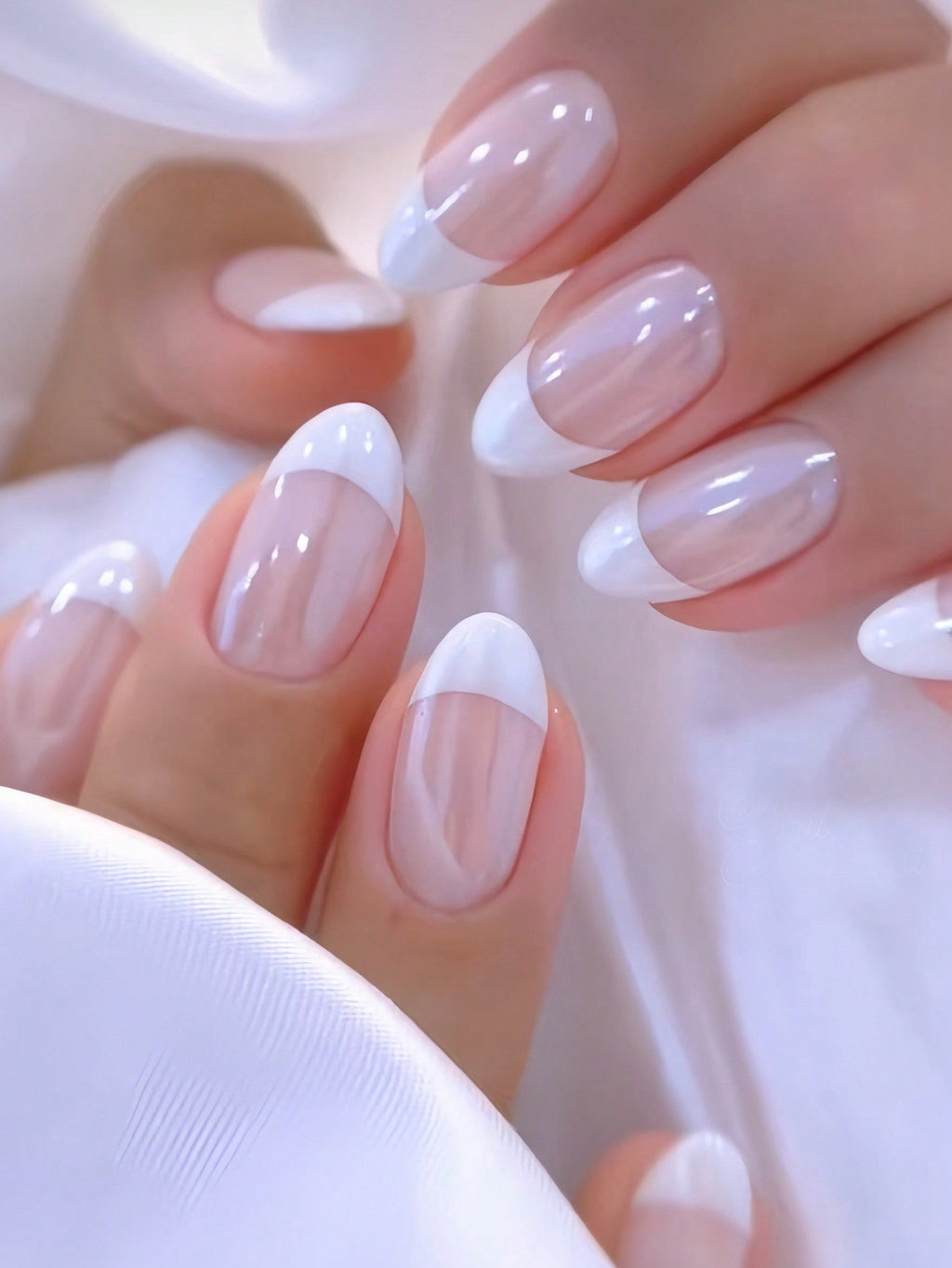 Close-up of a hand with almond-shaped nails painted in white and beige on a light background.