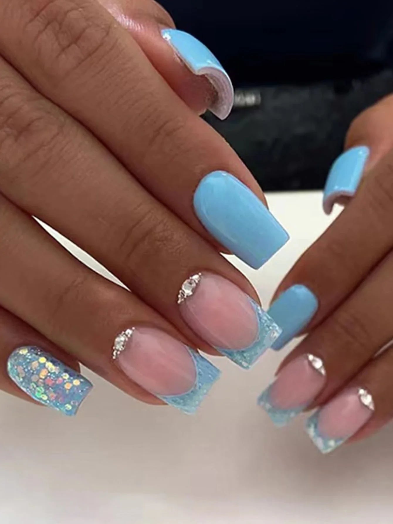 Close-up of hands with blue and pink nail polish on a neutral background