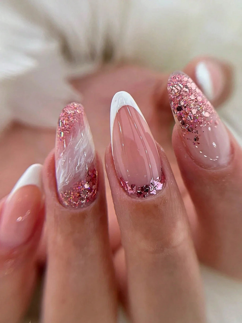 Close-up of a hand with pink and white glittery nail polish on a blurred background