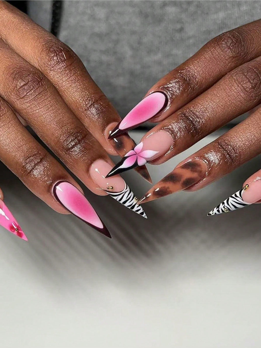 Close-up of hands with pink and zebra patterned nails on a neutral background