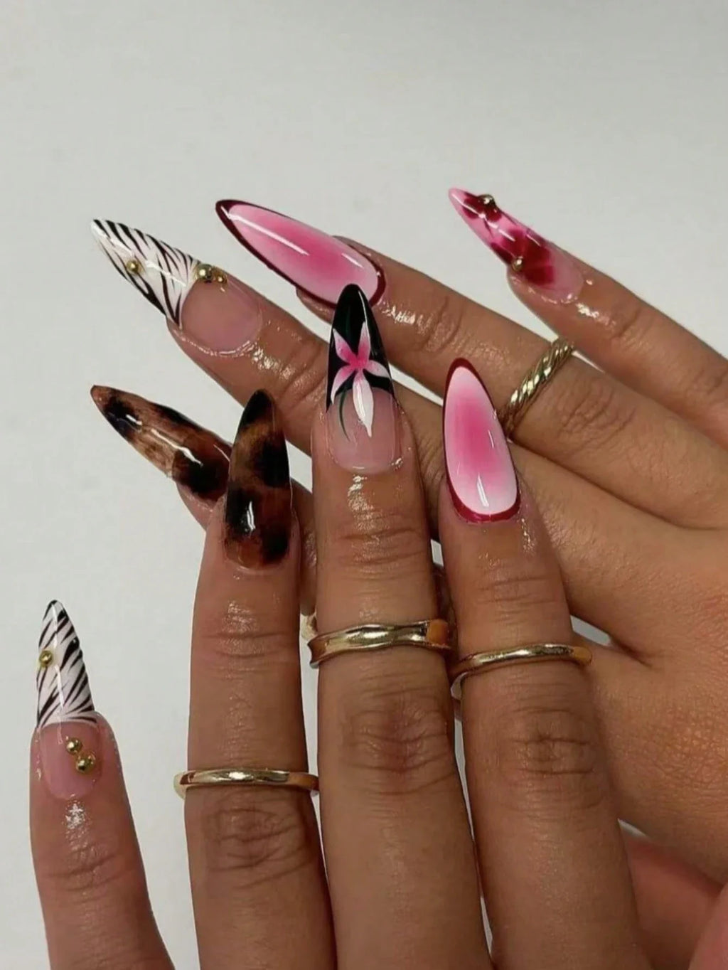 Nails with various designs including pink, black, and zebra pattern on a neutral background