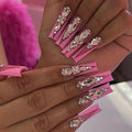 Hand with pink nail art designs featuring crystals and rhinestones.