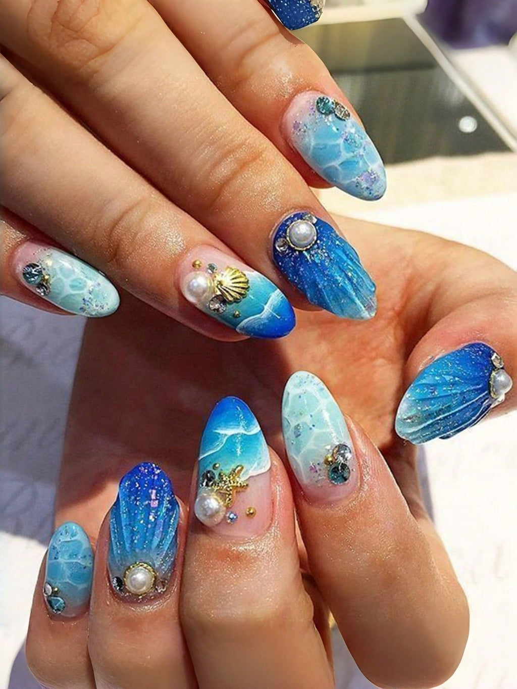 Nails with blue and white ocean-themed design featuring pearls and seashells.