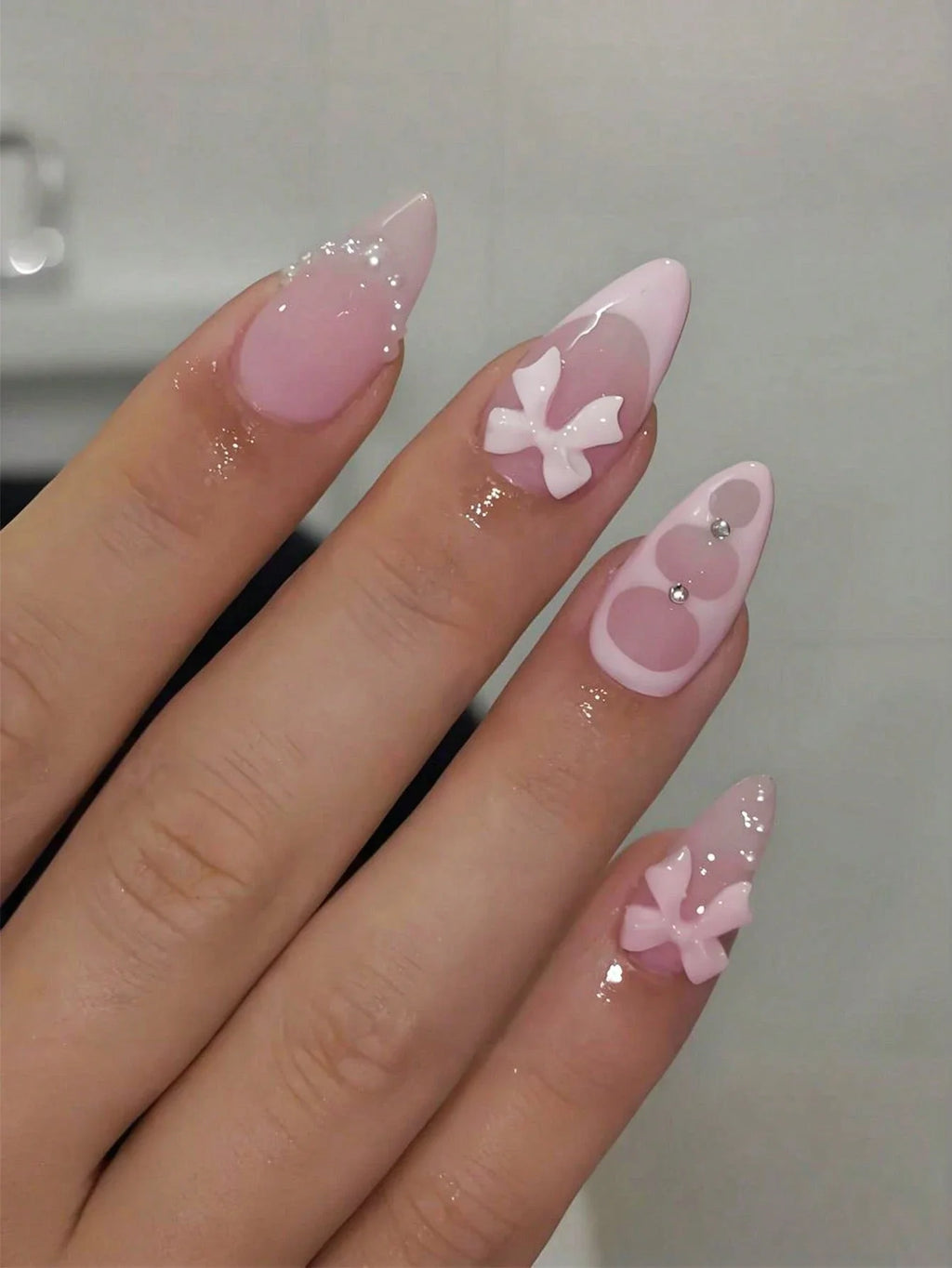 Hand with pink nail art featuring bow designs on a neutral background