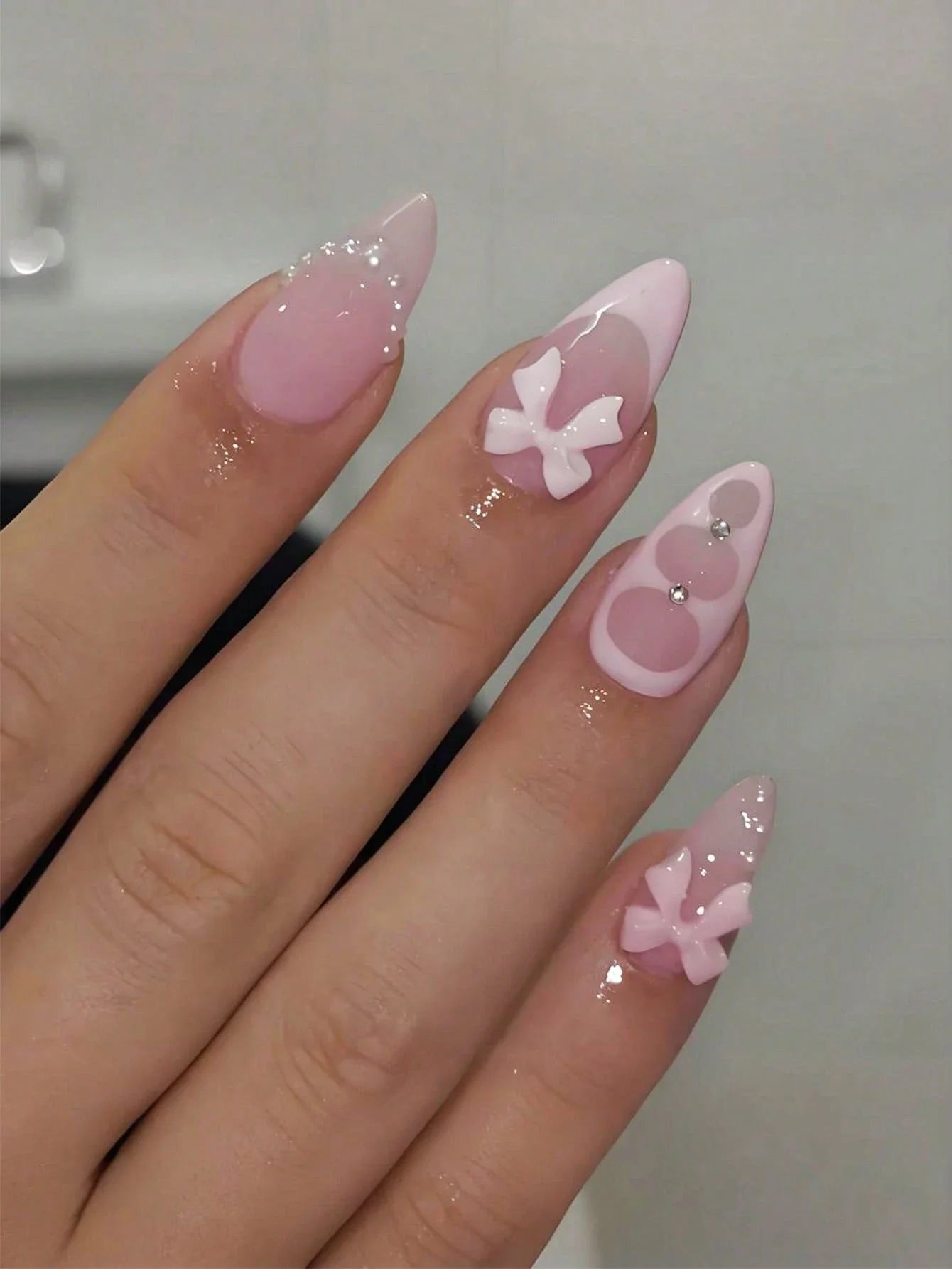 Hand with pink nail art featuring bow designs on a neutral background