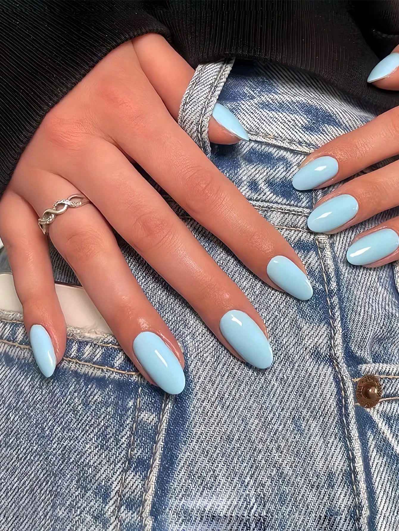 Close-up of hands with light blue nail polish on a denim background