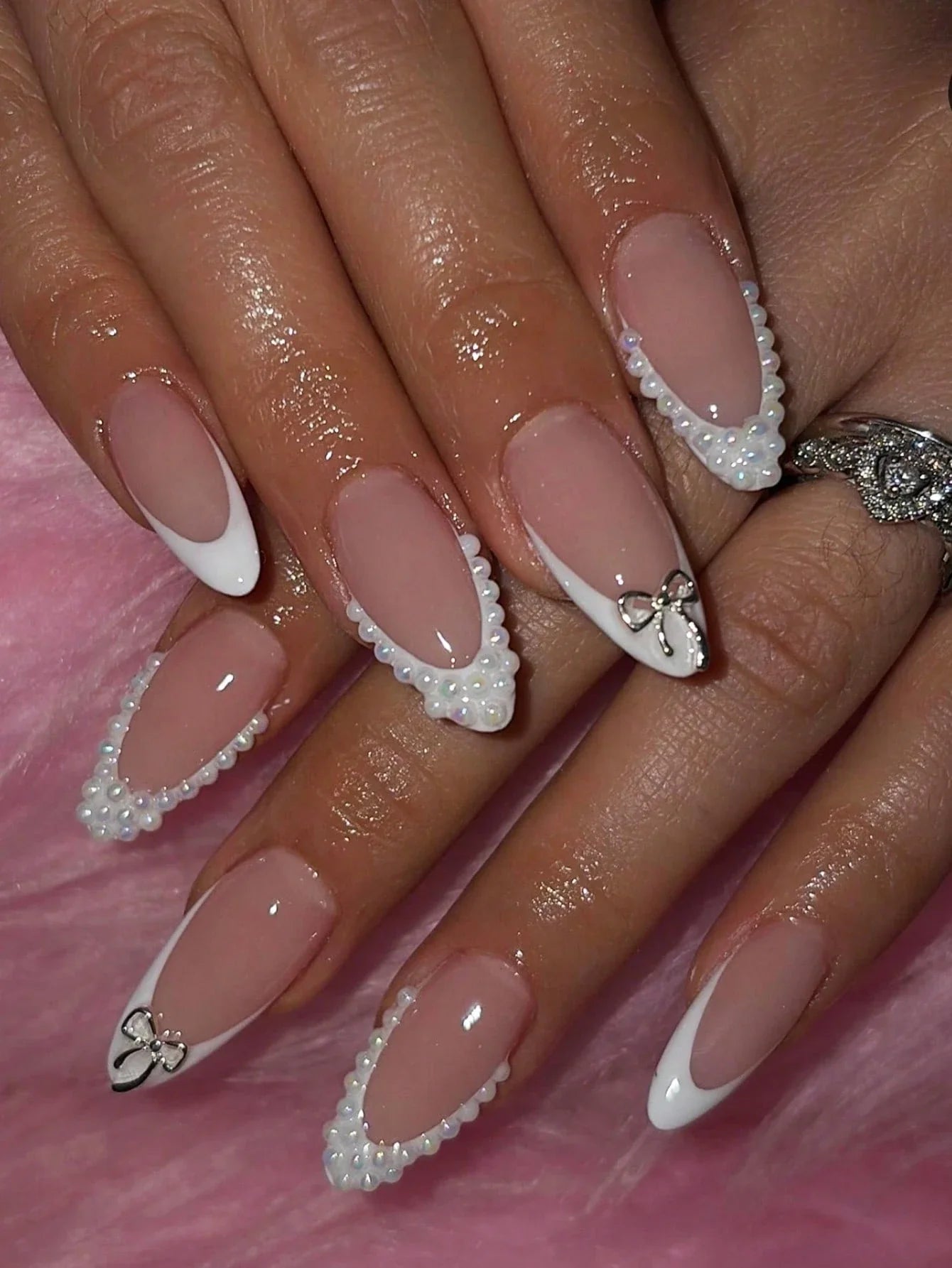 Nails with decorative bow and rhinestone design on a pink background